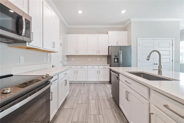 a kitchen with stainless steel appliances granite countertop a stove top oven a sink dishwasher and white cabinets with wooden floor