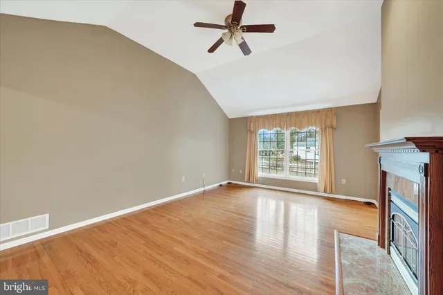 an empty room with wooden floor fan and windows