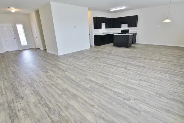 a view of kitchen and empty room with wooden floor