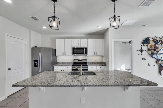 a kitchen with stainless steel appliances granite countertop a refrigerator a sink dishwasher a stove and white cabinets with wooden floor