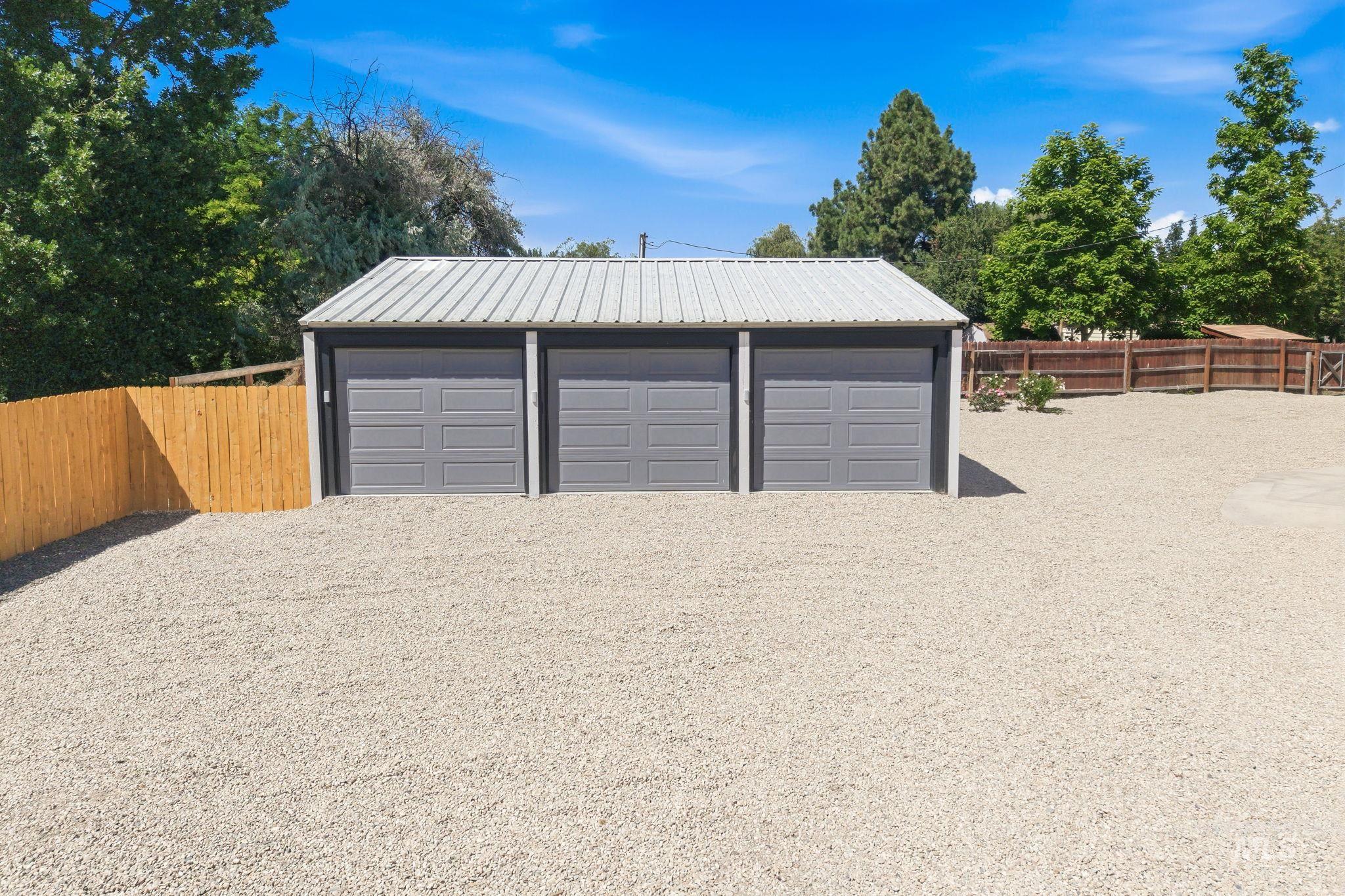 2152 Artesian Road Eagle, ID 83616 - Photo 38 of 50 Triple-bay garage with corrugated metal roofing, individual gray garage doors, and a light gravel driveway