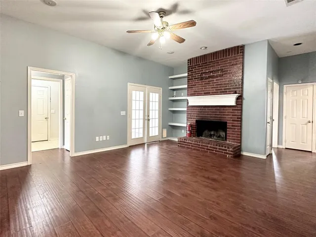a view of an empty room with wooden floor fireplace and a window