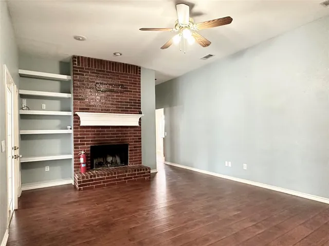 a view of an empty room with wooden floor fireplace and a window