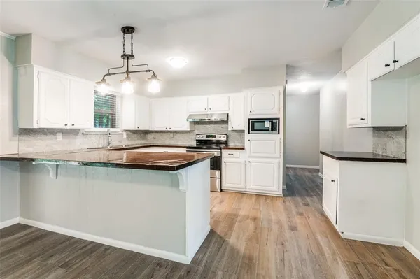 a kitchen with stainless steel appliances granite countertop a sink a stove a refrigerator and island with wooden floor