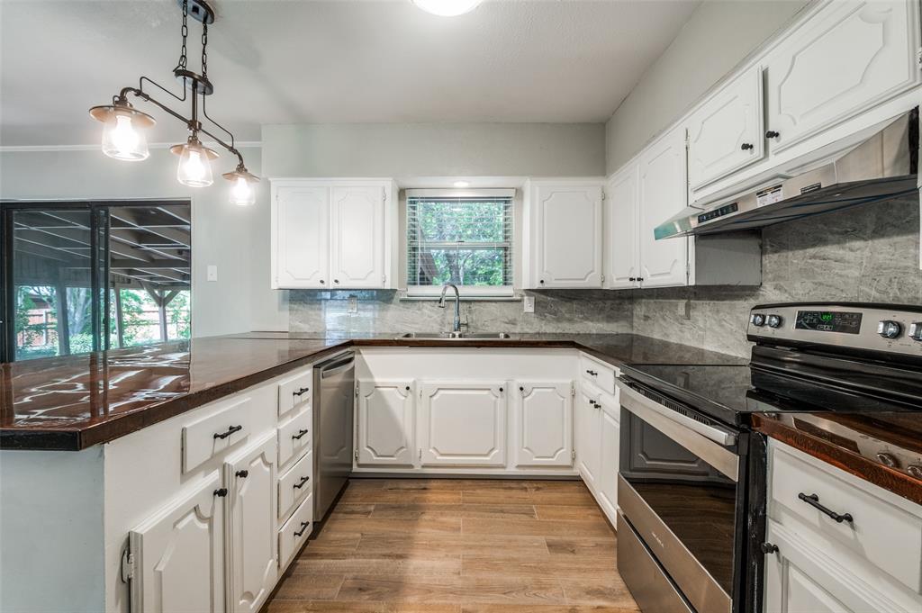 1533 East Springcrest Circle Lancaster, TX 75134 - Photo 12 of 25 U-shaped kitchen featuring white cabinetry, dark countertops, stainless steel appliances, and wood-finish flooring
