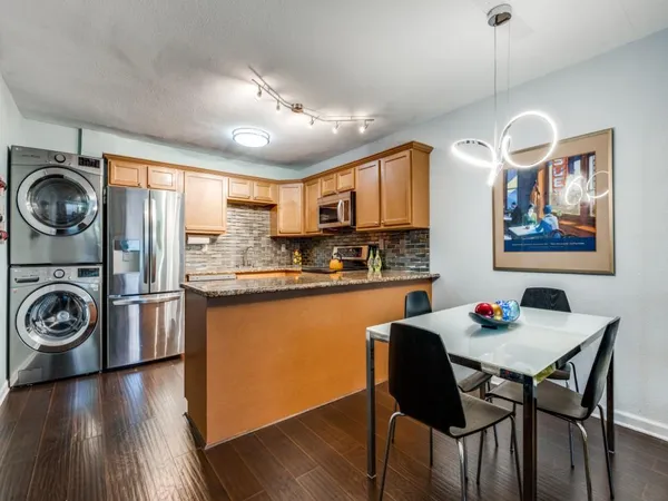 a kitchen with stainless steel appliances granite countertop a stove top oven a refrigerator a dining table and chairs with wooden floor