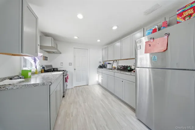 a kitchen with granite countertop a refrigerator a sink dishwasher and white cabinets with wooden floor