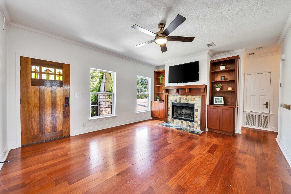 2108 Indian Creek Road Austin, TX 78734 - Photo 5 of 40 Unfurnished living room featuring hardwood / wood-style floors, crown molding, ceiling fan, built in features, and a textured ceiling