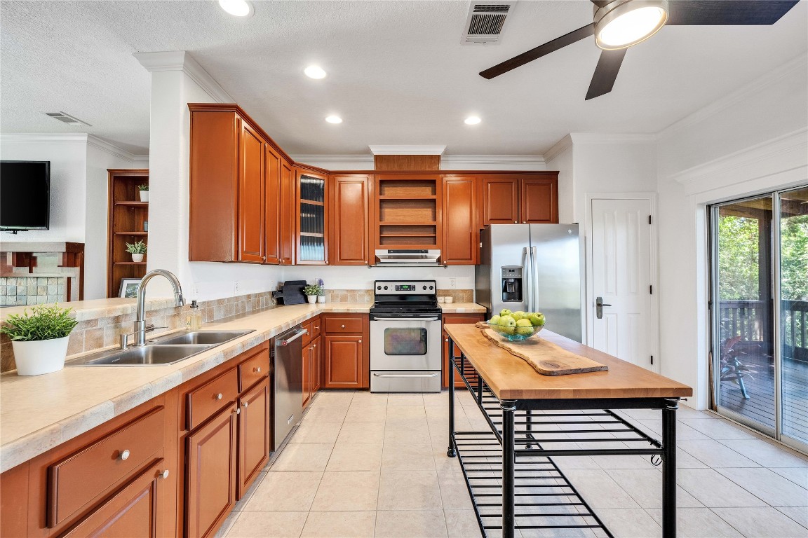 2108 Indian Creek Road Austin, TX 78734 - Photo 8 of 40 Kitchen featuring brown cabinetry, ornamental molding, open shelves, stainless steel appliances, and light countertops