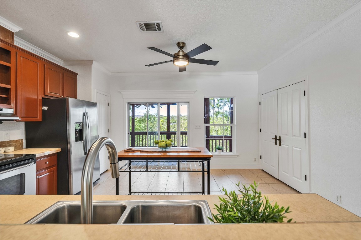 2108 Indian Creek Road Austin, TX 78734 - Photo 9 of 40 Kitchen with crown molding, light countertops, stainless steel appliances, light tile patterned flooring, and brown cabinetry