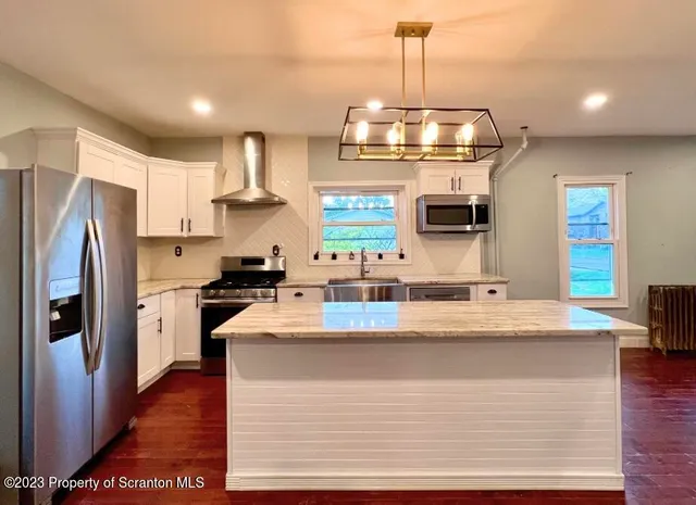 a kitchen with kitchen island granite countertop a refrigerator a stove a oven a sink dishwasher and wooden floor