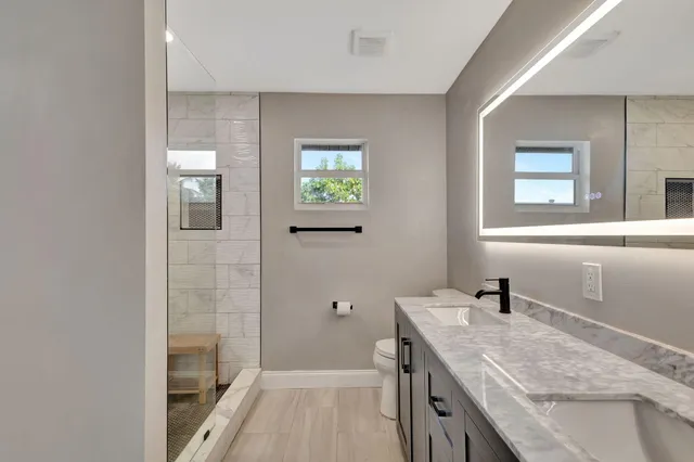 a bathroom with a granite countertop double vanity sink a mirror and a shower