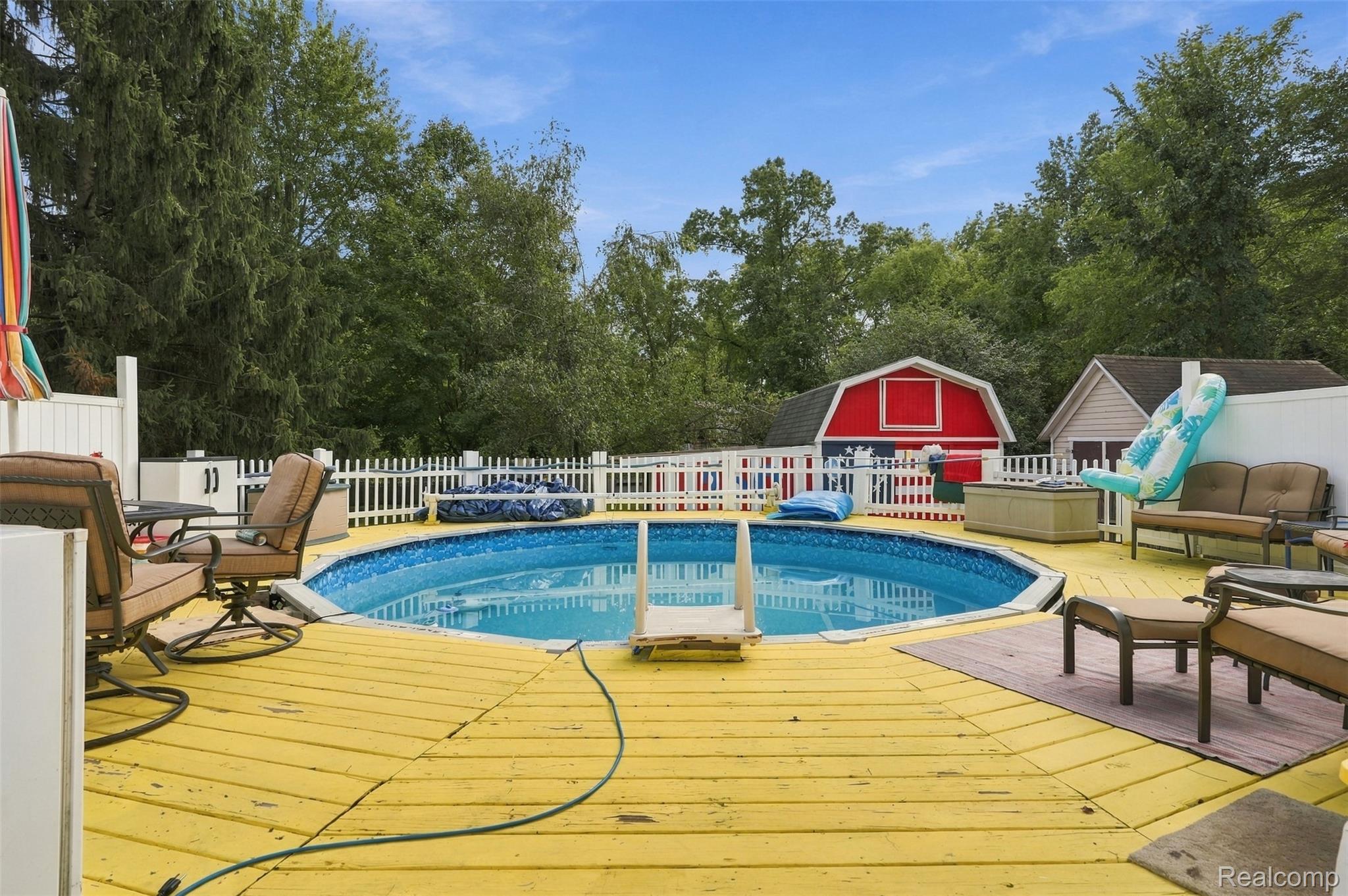 36739 Wick Road Romulus, MI 48174 - Photo 33 of 56 Outdoor above-ground pool surrounded by a bright yellow wood deck, white picket fencing, and mature trees