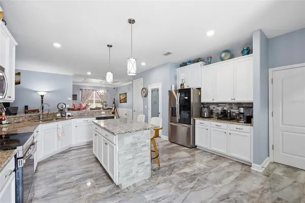 a kitchen with stainless steel appliances kitchen island granite countertop a refrigerator oven a sink dishwasher and white cabinets with wooden floor