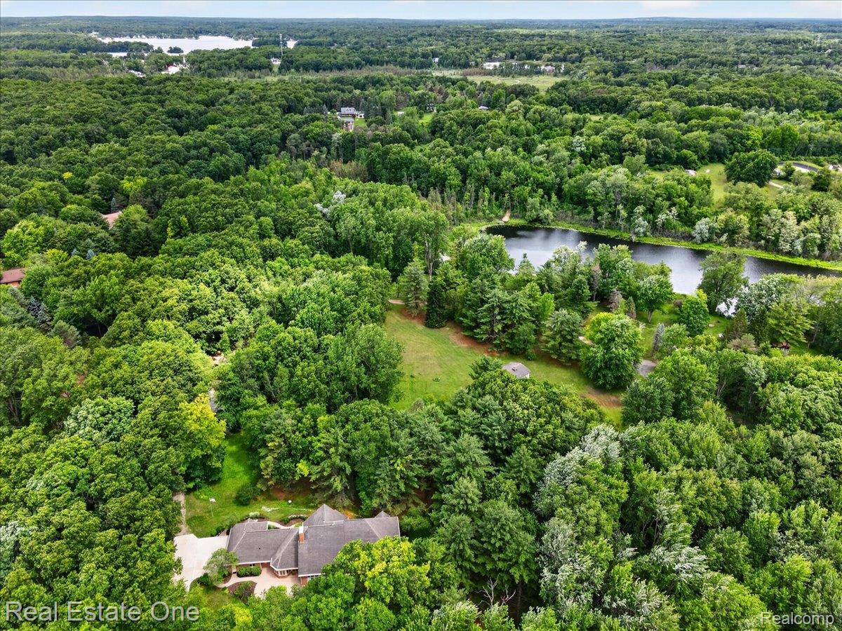 425 Courtney Road Leonard, MI 48367 - Photo 75 of 89 Expansive wooded landscape featuring a private pond and a secluded residence with a multi-gabled roofline