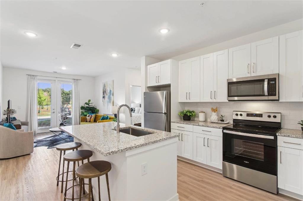 a kitchen with stainless steel appliances kitchen island granite countertop a stove top oven a sink dishwasher and a refrigerator with wooden floor