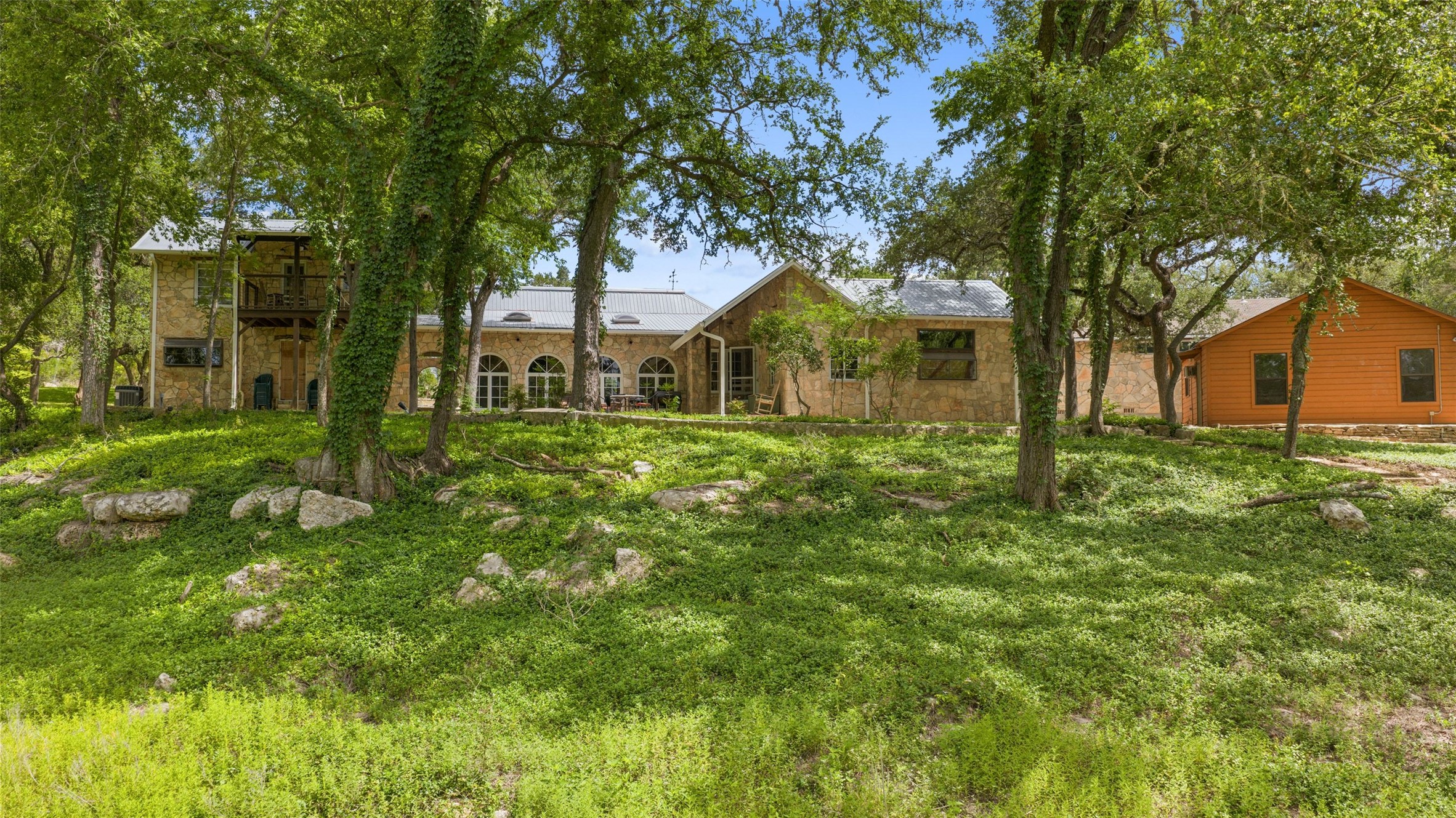 505 Red Corral Ranch Road Wimberley, TX 78676 - Photo 17 of 40 Lush landscaping surrounds this charming multi-level stone home with a metal roof and a detached wooden structure.