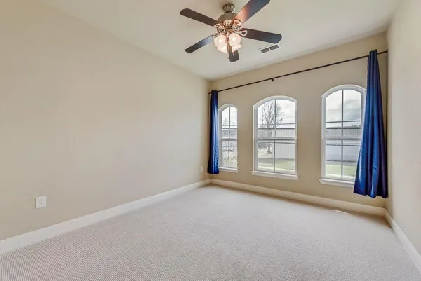 an empty room with chandelier fan and windows