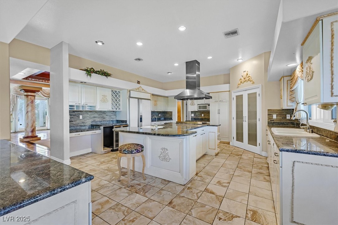 3372 Westwind Road Las Vegas, NV 89146 - Photo 26 of 39 Kitchen with decorative backsplash, dark stone countertops, white cabinetry, island exhaust hood, and a kitchen island