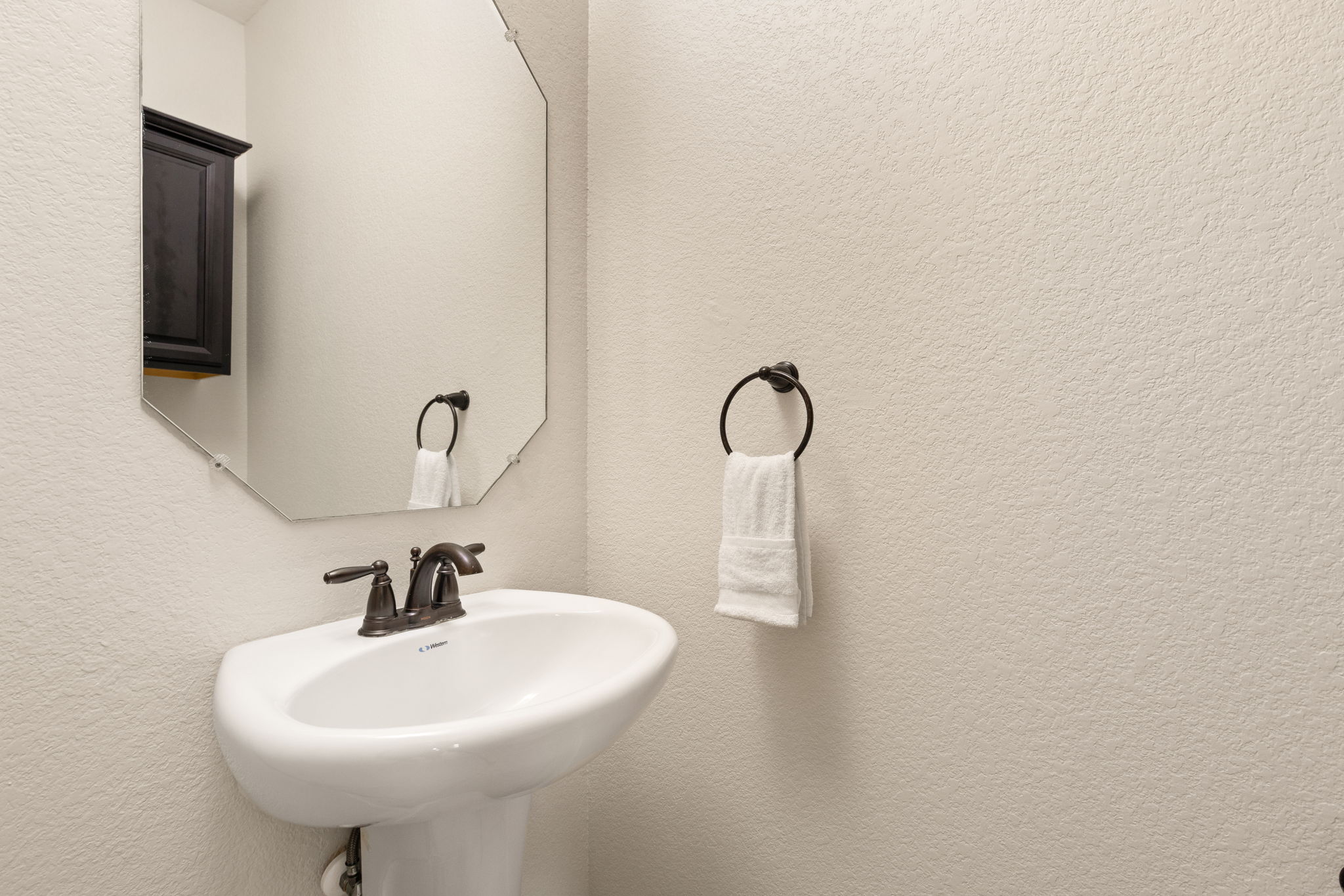 2400 Leonards Pass Leander, TX 78641 - Photo 19 of 40 A well-appointed powder room with a sleek pedestal sink and an elegant octagonal mirror.