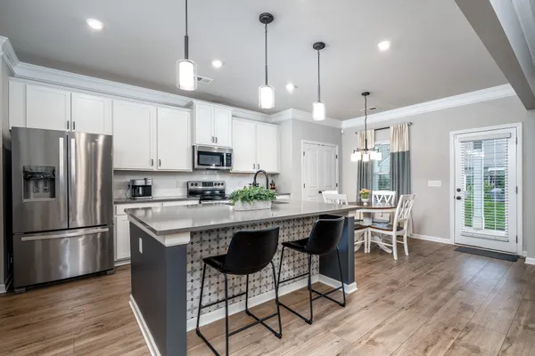 a kitchen with stainless steel appliances granite countertop a dining table chairs refrigerator and microwave