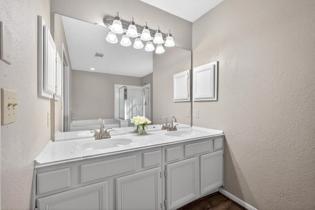 8815 Stoney Bend Drive Spring, TX 77379 - Photo 15 of 50 This bathroom features a double vanity with sleek faucets and a large mirror, complemented by modern light fixtures. The neutral walls and white cabinetry create a clean, bright atmosphere.