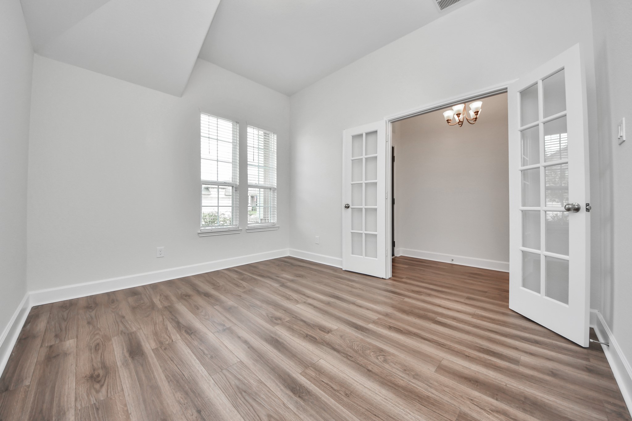 1614 Diamond Mountain Drive Rosharon, TX 77583 - Photo 4 of 40 This office/study room features elegant wood flooring, large windows for natural light, and French doors opening into an adjoining space with a chandelier, creating a bright and versatile area.