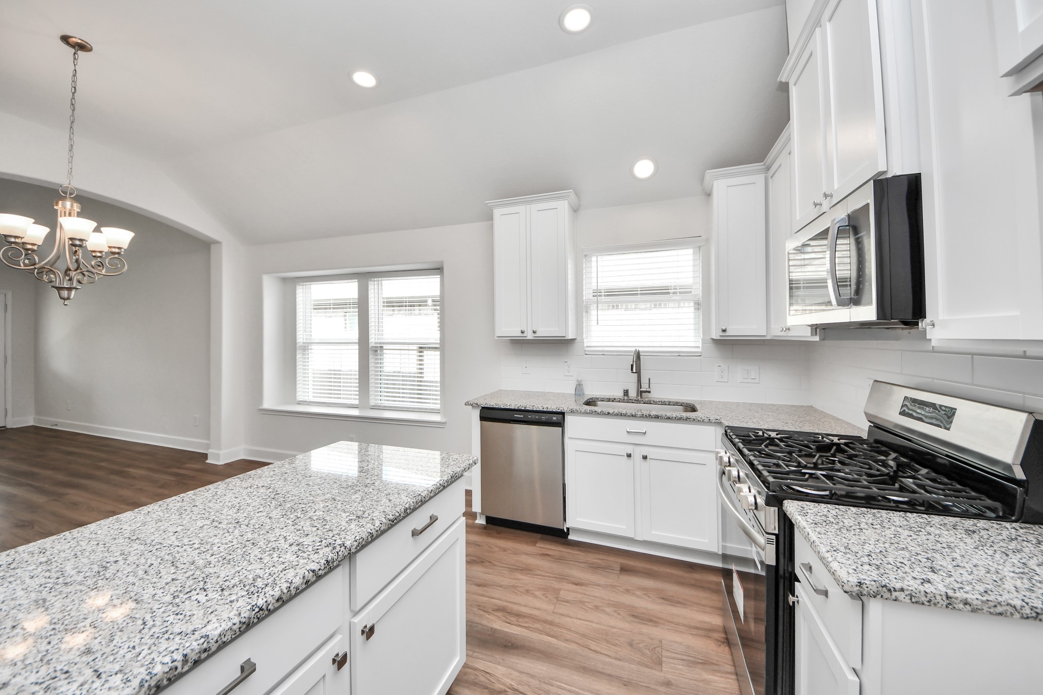 1614 Diamond Mountain Drive Rosharon, TX 77583 - Photo 10 of 40 This photo showcases a bright, modern kitchen with white cabinets, granite countertops, and stainless steel appliances. The space features an open layout with an adjacent dining area under a stylish chandelier and wood flooring throughout.