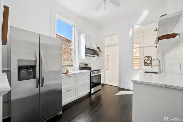 a kitchen with stainless steel appliances white cabinets a sink a stove a microwave and wooden floors