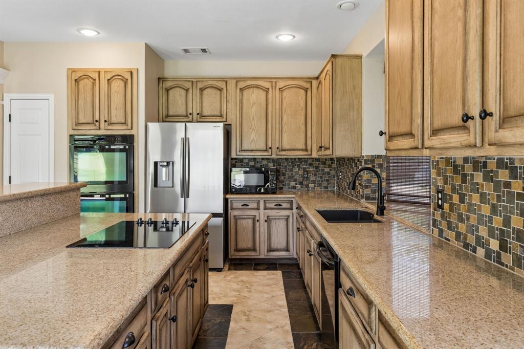 2925 Sunset Ridge McKinney, TX 75072 - Photo 12 of 33 Spacious gourmet kitchen featuring granite countertops, custom cabinetry, stainless steel and black appliances, decorative stone accents, and an oversized island ideal for cooking and entertaining.