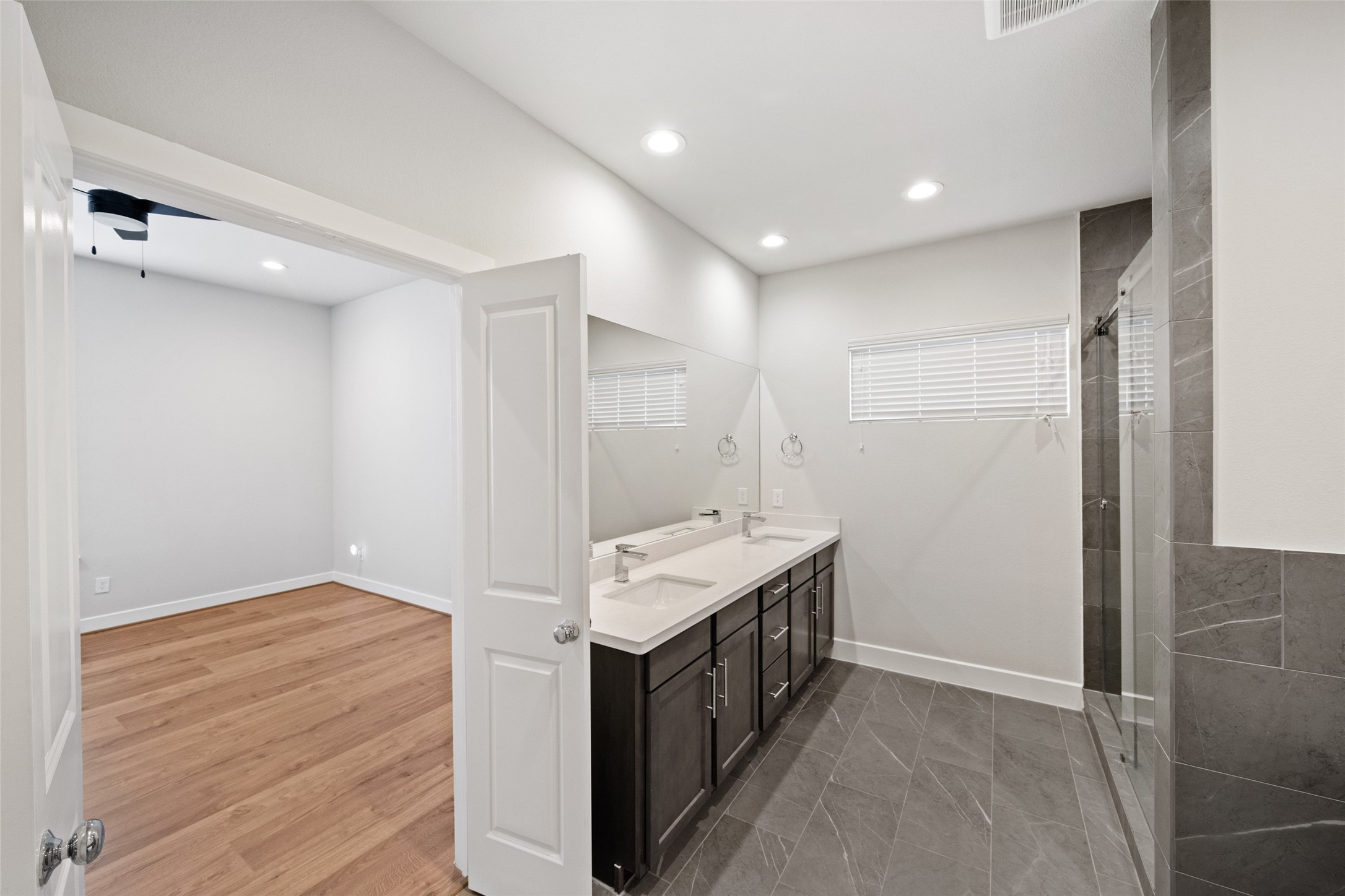 5910 Haring Lane Houston, TX 77091 - Photo 15 of 20 Modern primary bathroom with dual sinks, dark cabinetry, and a spacious glass-enclosed shower. It connects to a room with hardwood flooring, providing a seamless transition between spaces. The neutral color palette and recessed lighting add to the contemporary feel.