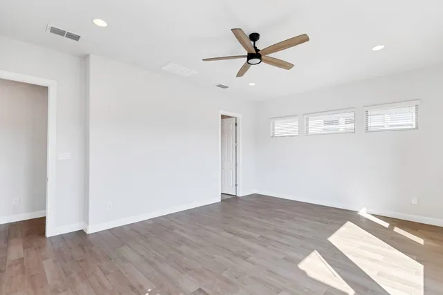 a view of a big room with wooden floor a ceiling fan and windows