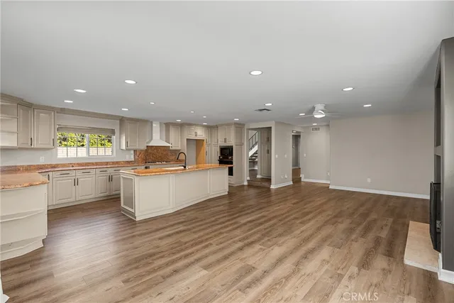 a large white kitchen with a white countertops a stove a couch and a dining table with wooden floor
