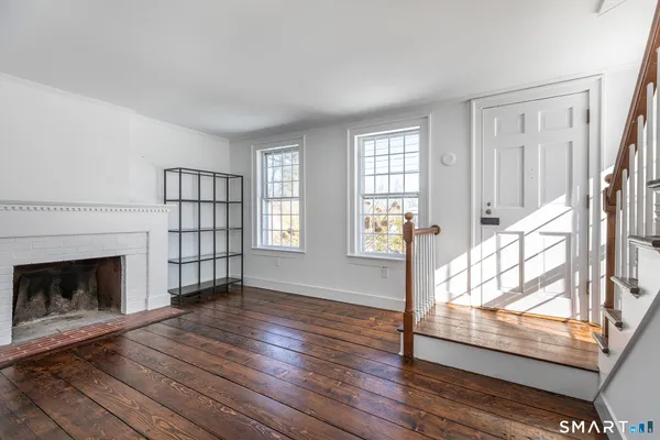a view of an empty room with wooden floor fireplace and a window