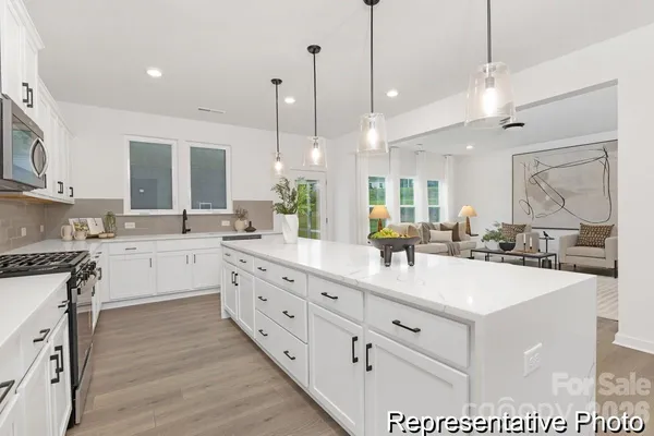 a large white kitchen with kitchen island a large counter space a sink stainless steel appliances and cabinets