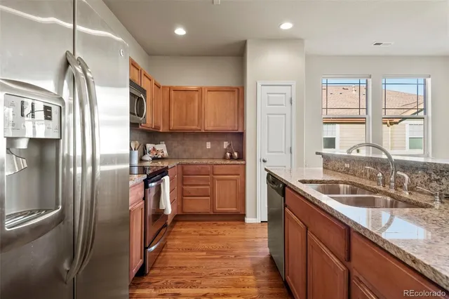a kitchen with granite countertop a refrigerator a sink a stove and wooden cabinets