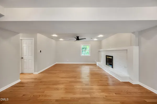 a view of an empty room with wooden floor and a kitchen