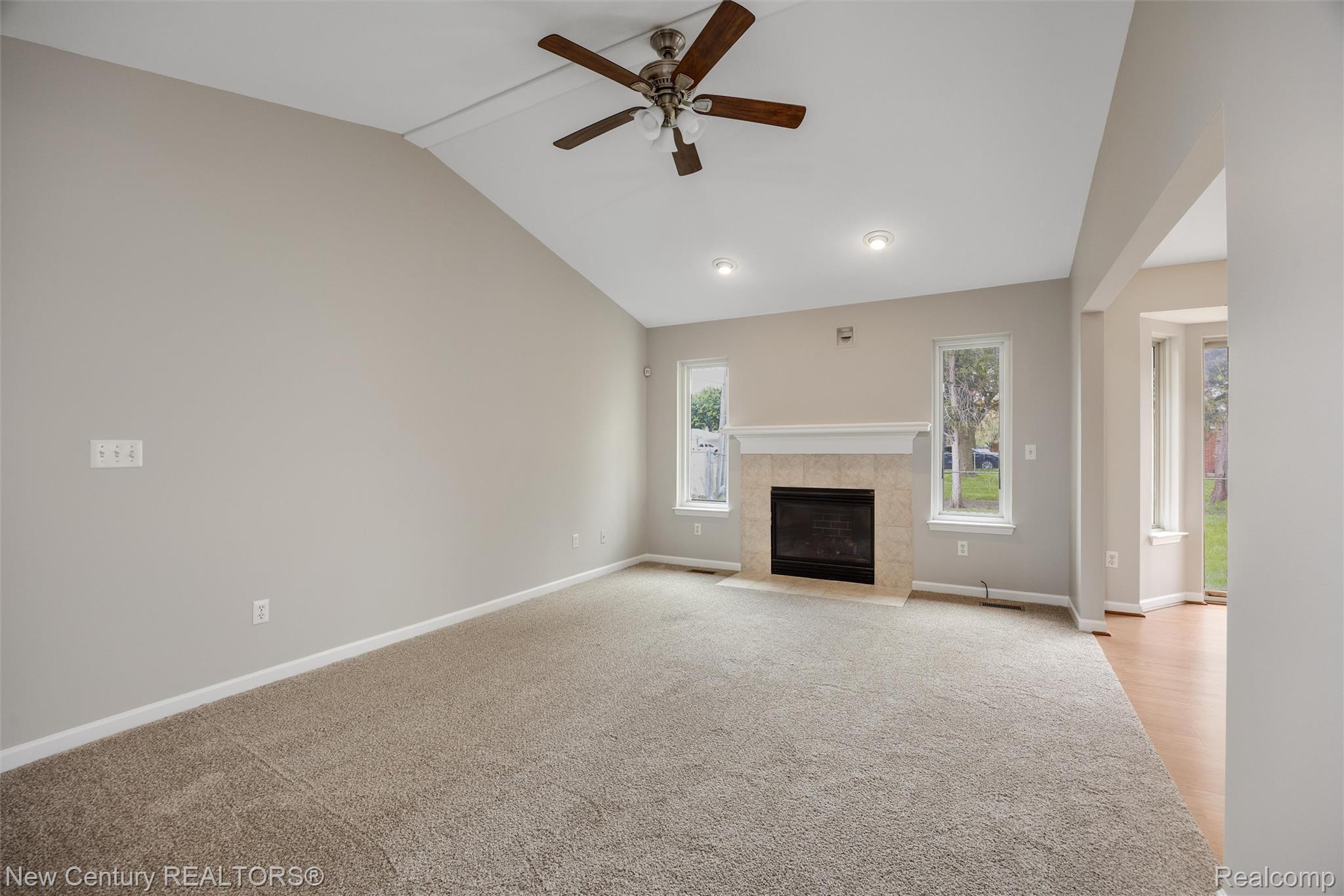 26013 Ranger Avenue Warren, MI 48091 - Photo 4 of 25 Unfurnished living room with a ceiling fan, vaulted ceiling, a tile fireplace, and light colored carpet