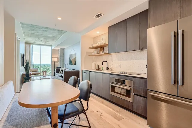 a kitchen with stainless steel appliances granite countertop a refrigerator a stove a sink dishwasher a dining table and chairs with wooden floor