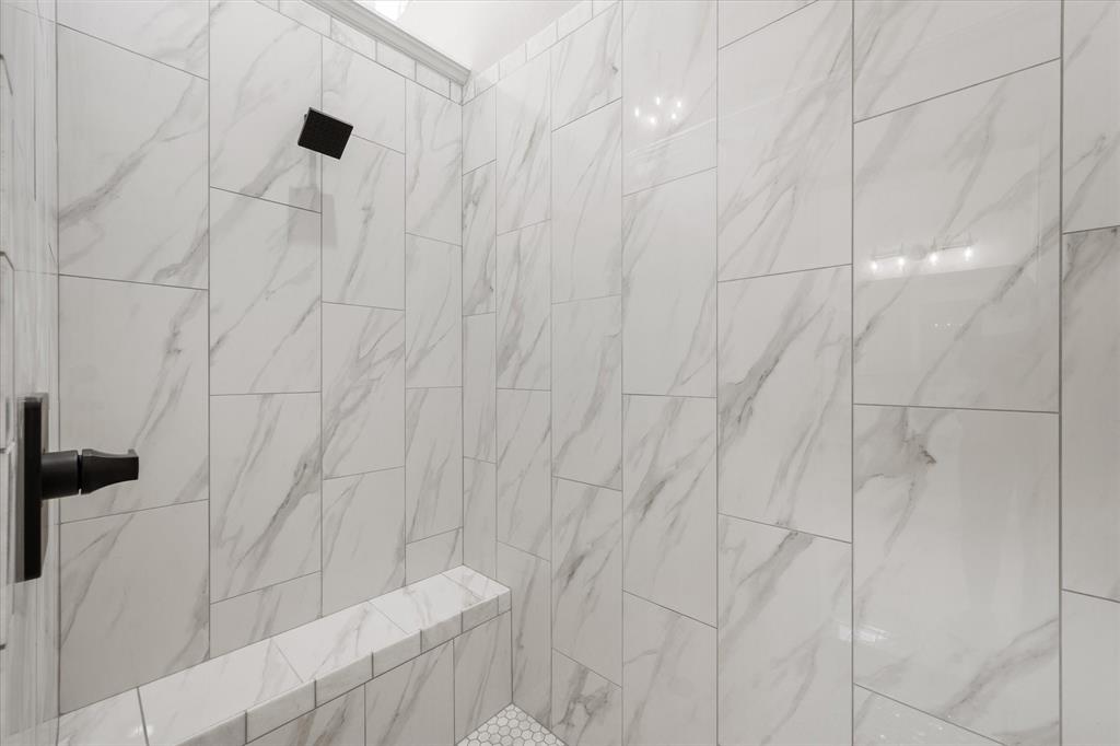 6610 Waggoner Way Midlothian, TX 76065 - Photo 21 of 40 Shower enclosure featuring floor-to-ceiling white marble-look tile, a built-in bench, matte black showerhead, and matte black lever handle