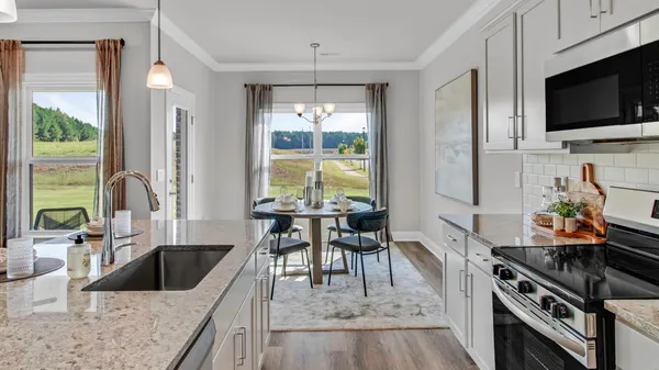 a kitchen with stainless steel appliances granite countertop a stove top oven a sink a dining table and chairs with wooden floor