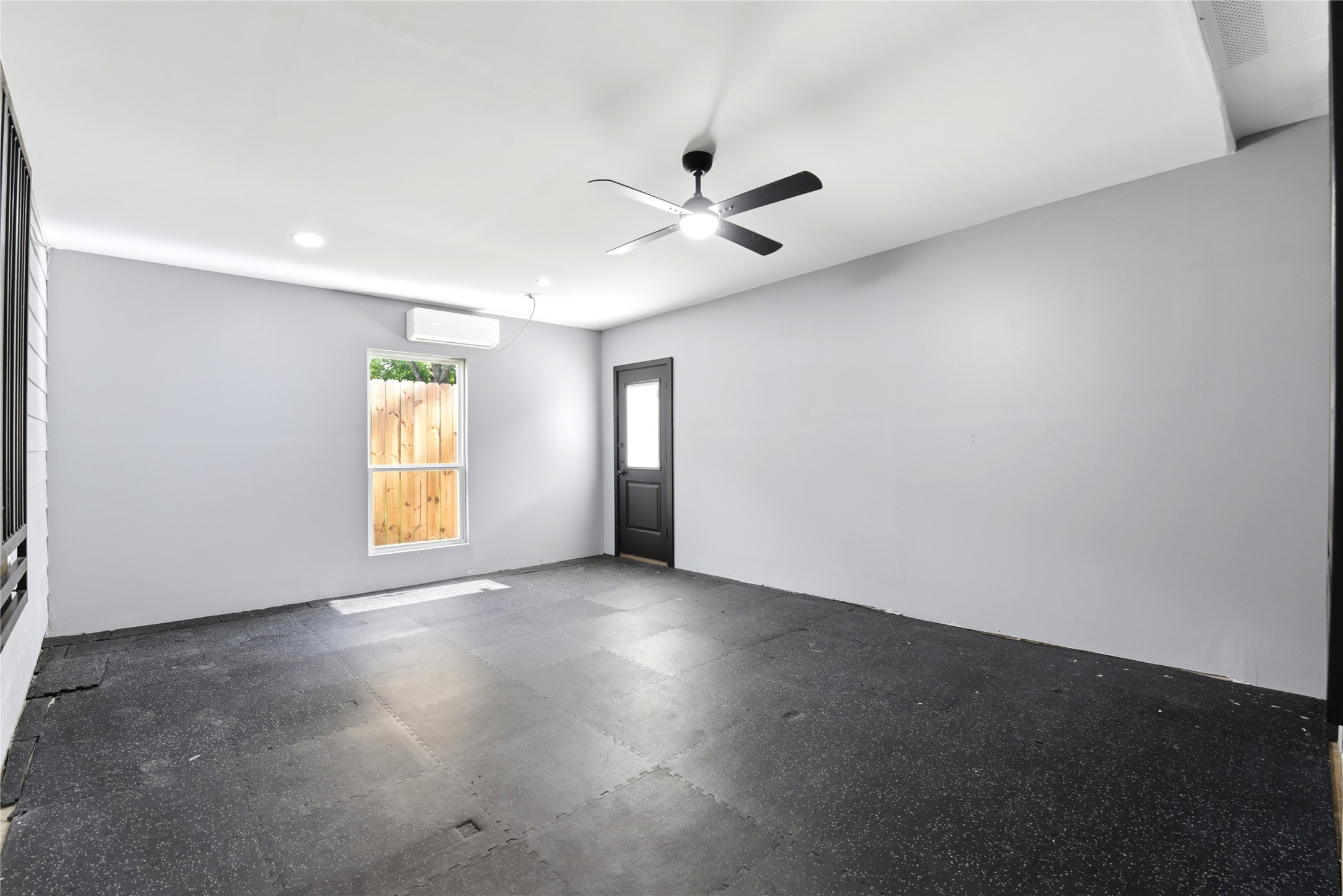 9403 Spaulding Street Houston, TX 77016 - Photo 30 of 50 This room has a modern feel with light gray walls, a ceiling fan, and recessed lighting. It features a window and a door leading outside, offering natural light and easy access. The dark flooring adds contrast, perfect for versatile use.