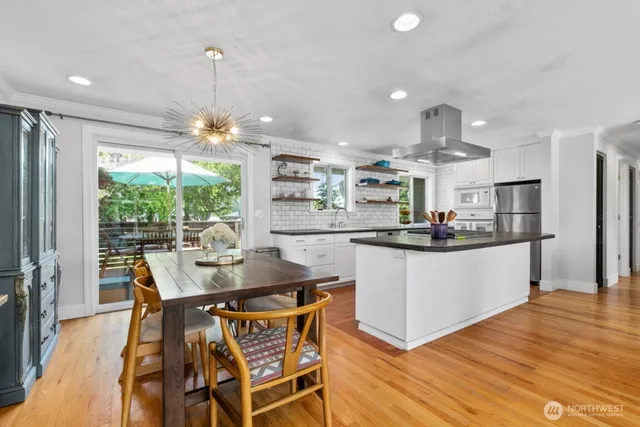 a kitchen with stainless steel appliances kitchen island granite countertop a table chairs and a wooden floor