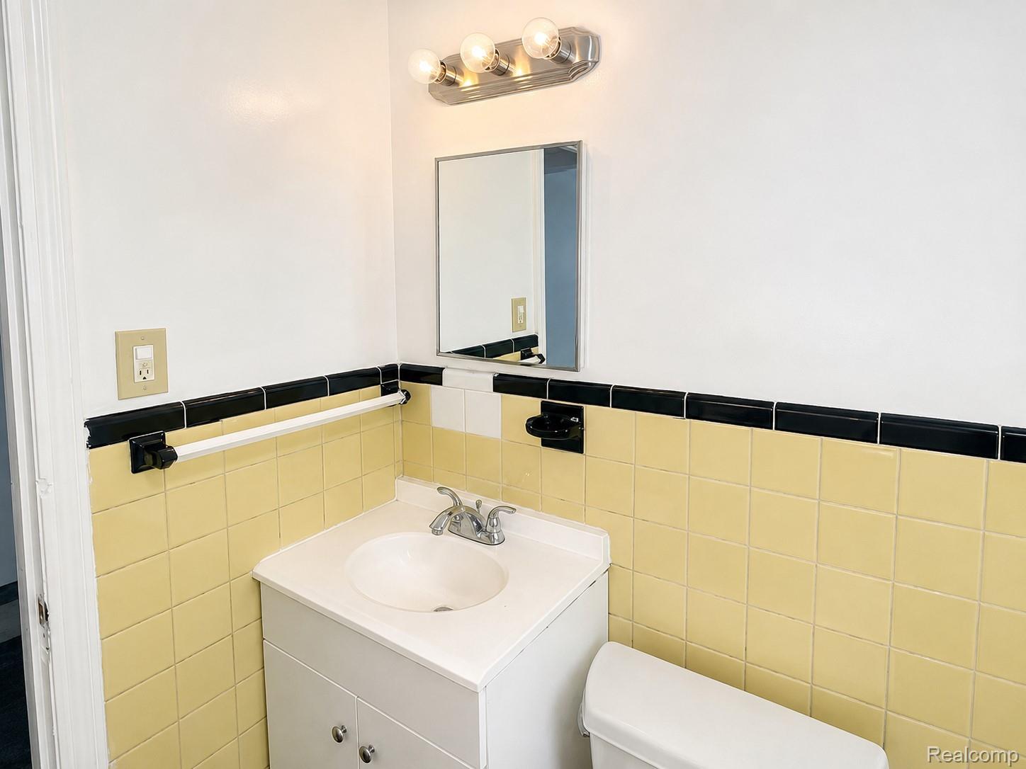 13590 Rutherford Street Detroit, MI 48227 - Photo 5 of 10 Bathroom featuring a white vanity with integrated sink, coordinating white toilet, yellow and black tiled walls, and a wall-mounted light fixture