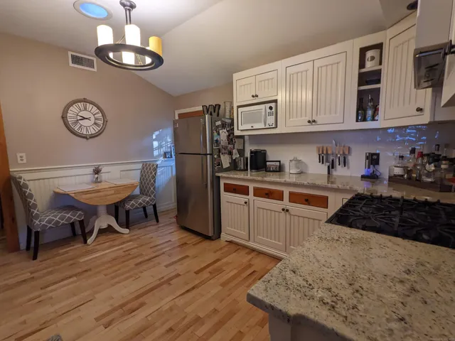 a kitchen with stainless steel appliances granite countertop a stove top oven a refrigerator a dining table and chairs with wooden floor