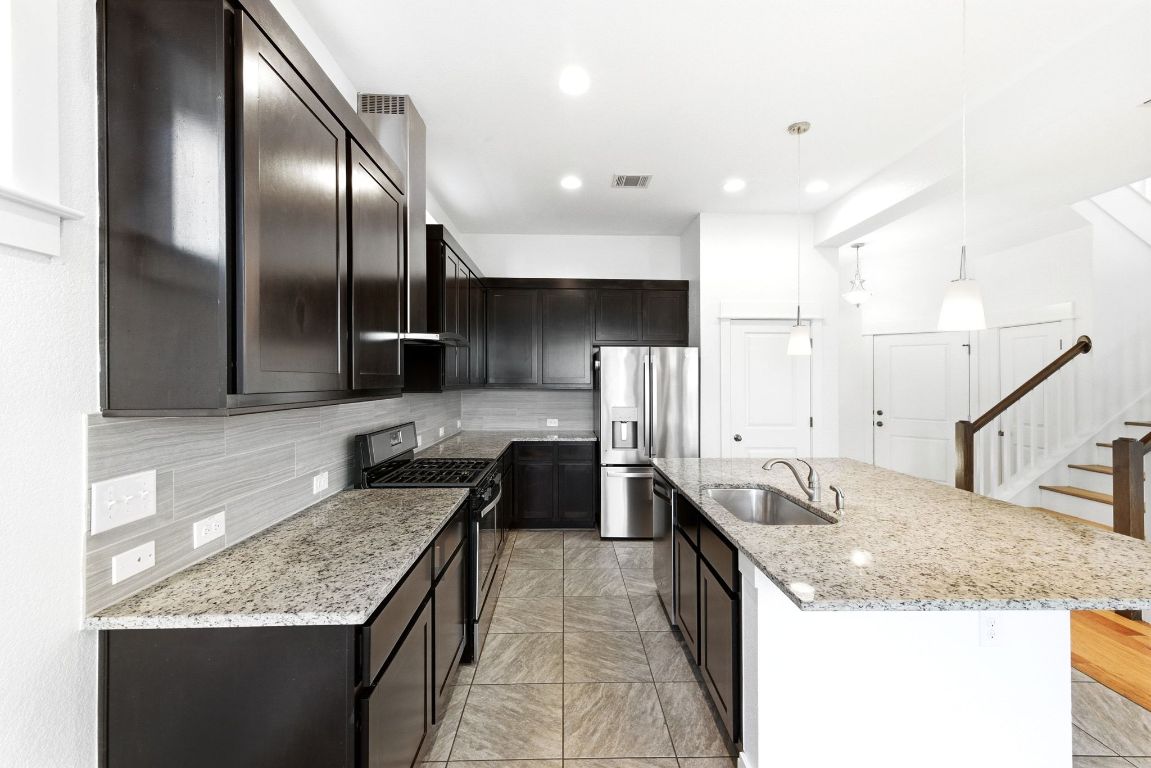 1912 Haskell Street, Unit 1 Austin, TX 78702 - Photo 7 of 23 Kitchen featuring stainless steel appliances, light stone countertops, hanging light fixtures, and decorative backsplash