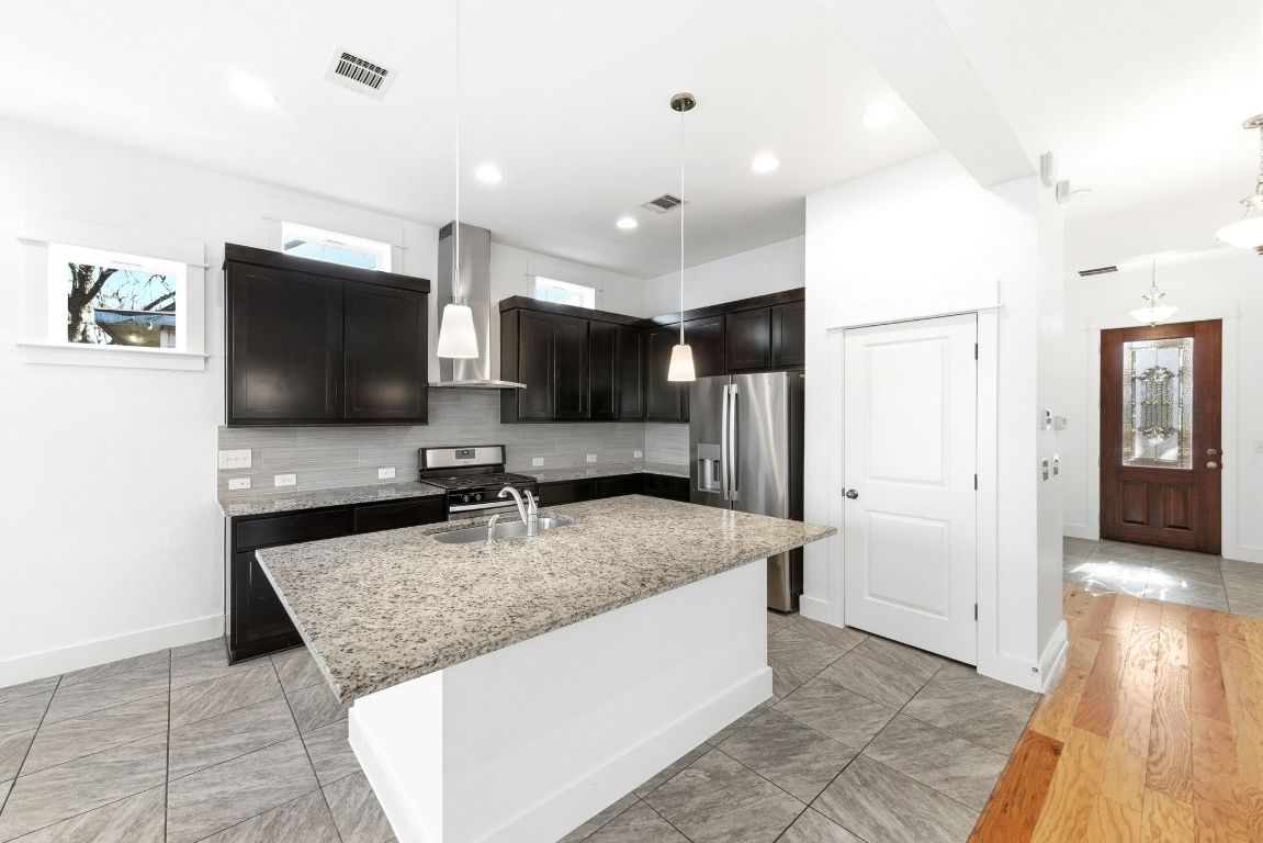 1912 Haskell Street, Unit 1 Austin, TX 78702 - Photo 8 of 23 Kitchen featuring wall chimney exhaust hood, light stone counters, stainless steel appliances, a kitchen island with sink, and pendant lighting