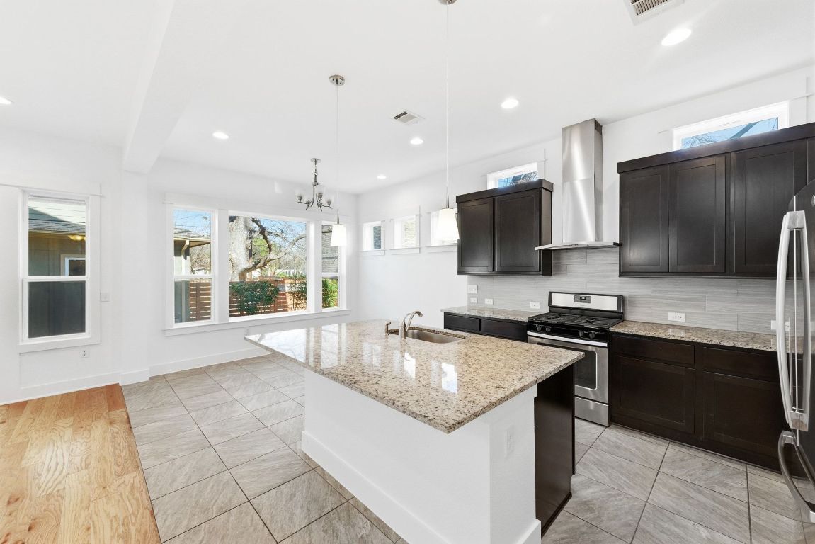1912 Haskell Street, Unit 1 Austin, TX 78702 - Photo 9 of 23 Kitchen with backsplash, stainless steel appliances, light stone counters, an island with sink, and decorative light fixtures