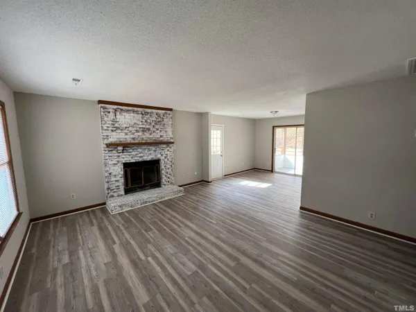 an empty room with wooden floor fireplace and windows