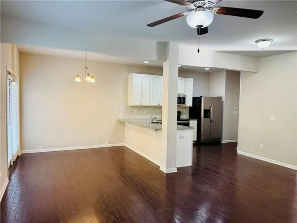 an empty room with wooden floor a ceiling fan and kitchen view